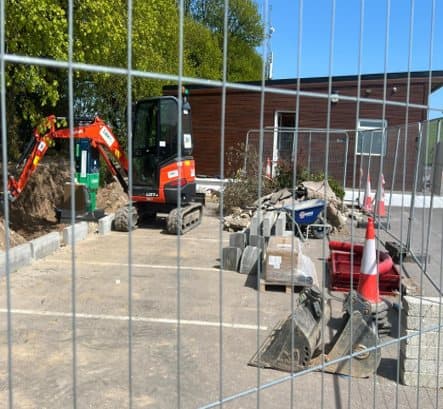 Mini excavator working behind safety fencing in the golf course car park