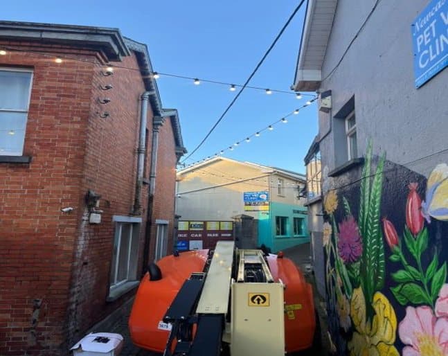 Festoon lighting and access equipment on a lane beside a painted mural
