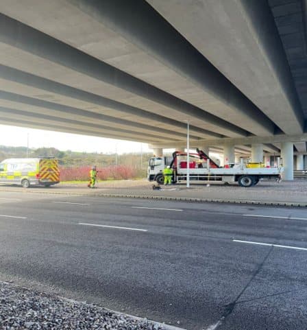 Maintenance crew and vehicles working beneath a motorway overbridge
